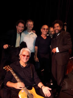 Jeff, wearing dark glasses, holding guitar, seated in wheelchair with his band the Rev. Dr. Cornel West at Poverty Tour 2.0, Cleveland Ohio. Jeff has his arm extended In a welcoming, inclusive gesture. 2012. Photo by Ed Lemmer.