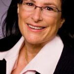 Caucasian woman with dark brown hair, pink blouse and dark suit smile into the camera.