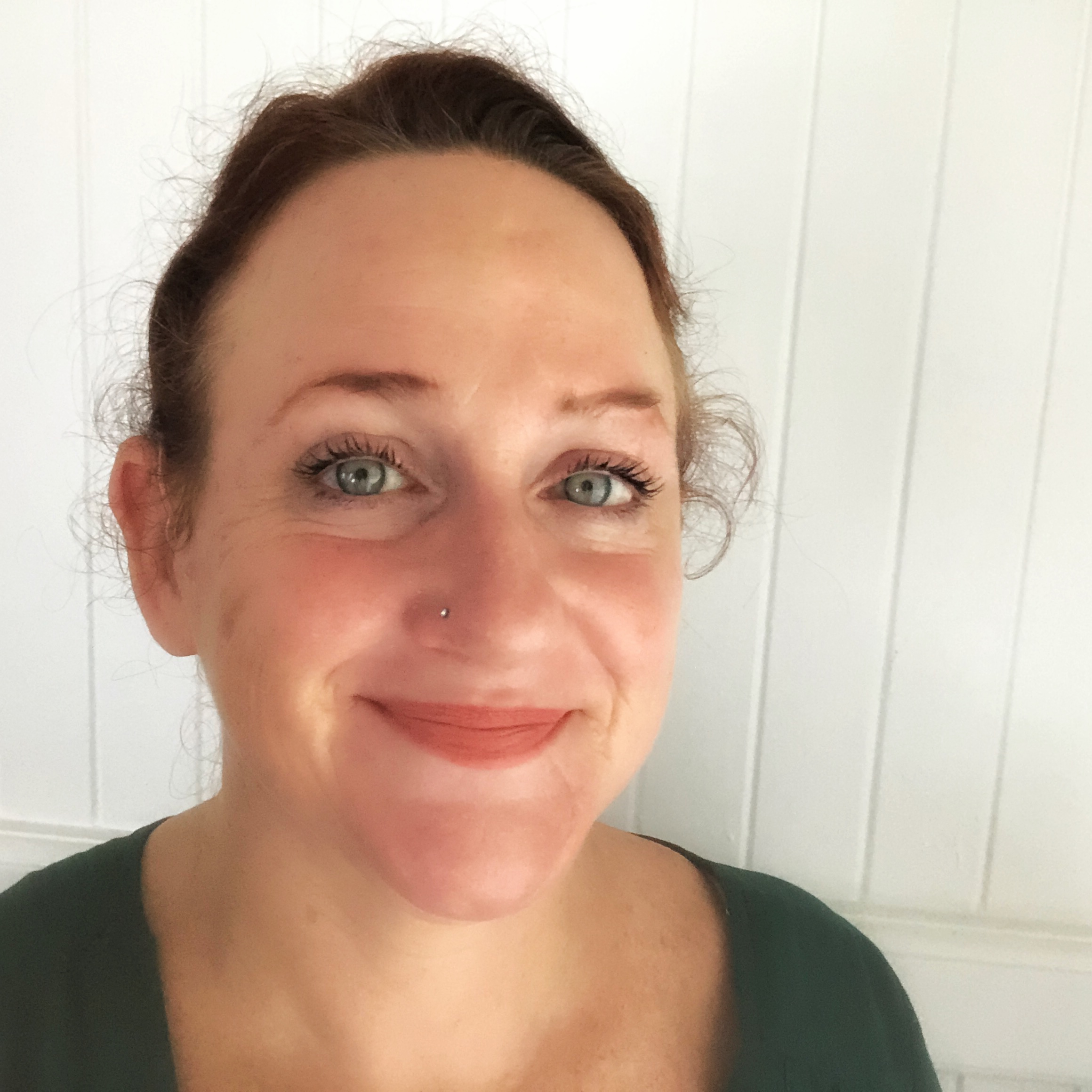 A white woman with dark hair looks at the camera and smiles. Her eyes are blue and she appears friendly