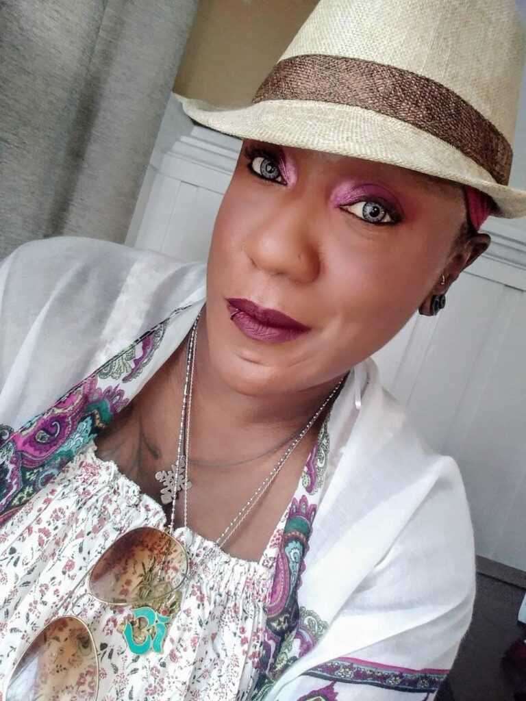 African American woman with a beige fedora and white outfit with Paisley pattern along the edges.