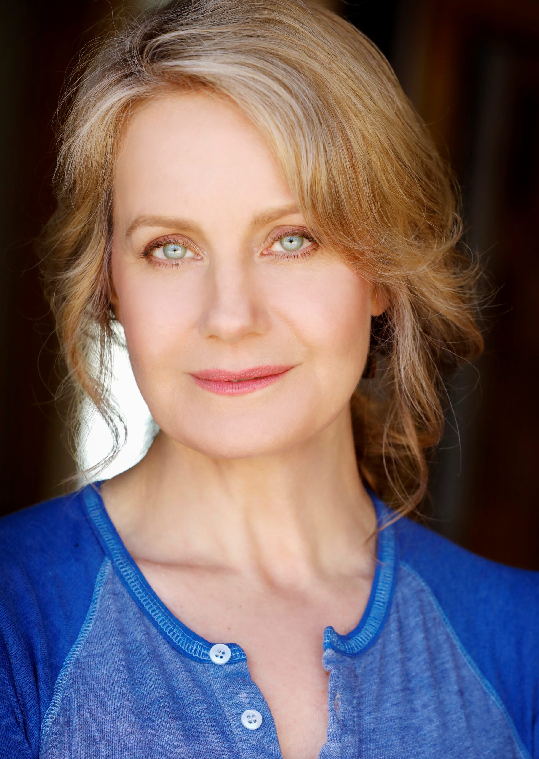 Actress, Eileen Grubba, blonde wavy hair, pulled back, light blue eyes, wearing a blue t-shirt, and a slight smile.